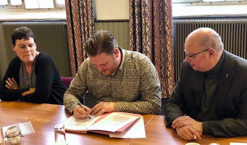 Onder toeziend oog van pastoor Maickel Prasing tekent wethouder Thomas Melisse de overeenkomst.