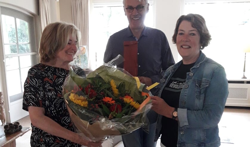 Voorzitter Maria van Nispen overhandigt de jubilaris een boekt bloemen.